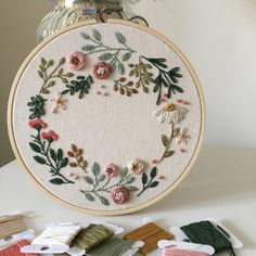 a cross stitch wreath with flowers and leaves in the center on a table next to some scissors