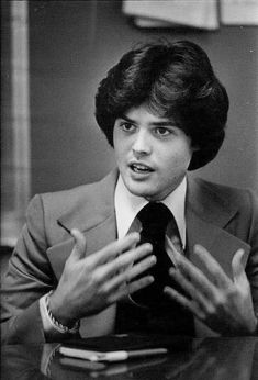 a man in a suit and tie sitting at a table with his hands out to the side