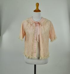 This lovely peachy pink lace bed jacket features off white lace ruffle edges, and insert ribbon reminiscent of Odette Barsa's designs. It is lined in nylon knit. LABEL: MIstee. Medium ( see measurements) All Nylon. Made in USA. Hand Wash CONDITION: excellent plus without issues / hand laundered MEASUREMENTS: suitable sizes small to medium shoulder to shoulder: 14 in. bust: 36 in. length: 19 in. sleeve length: 10 in. Vintage Pink Jacket, Pink Ruffled Lace Top, Pink Lace Top With Ruffles, Feminine Pink Lace Top With Lace Patchwork, Pink Lace Top With Ruffles For Spring, Feminine Pink Lace Top With Patchwork, Pink Lace Top With Lace Patchwork, Spring Pink Lace Top With Patchwork, Pink Lace Top With Patchwork For Spring