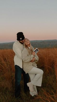 a man and woman hugging in the middle of a field with tall grass at sunset