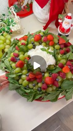 a wreath made out of grapes and strawberries on a table with santa clause in the background