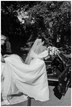 a woman in a wedding dress getting out of a car with her veil pulled back