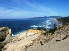 a view of the ocean and beach from a cliff side area with sand dunes on both sides