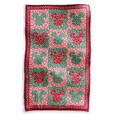 a red and green patchwork quilt with cherries on the front, hanging from a white wall