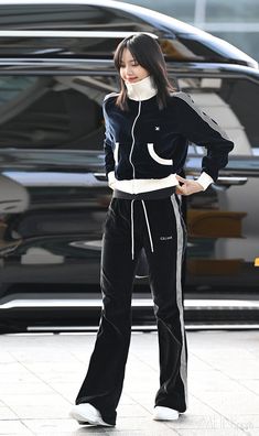 a woman in black and white tracksuits is walking down the street with her hand on her hip