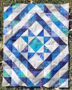 a blue and white quilt sitting on top of the grass in front of some leaves