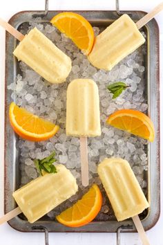 popsicles with orange slices and mint on ice in a metal tray surrounded by crushed up sea salt