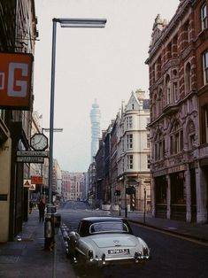 an old car is parked on the side of the road in front of tall buildings