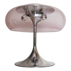 a pink glass table lamp sitting on top of a metal base with three lights in the middle