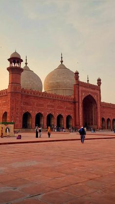 people are walking around in front of a large red building with two domes on top