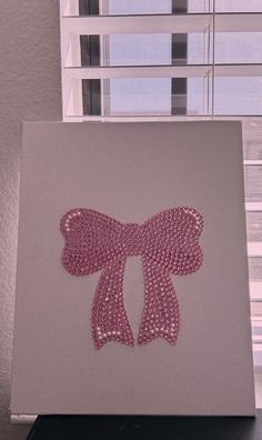 a pink bow on a white canvas in front of a window