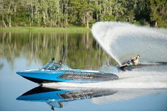 two people on a speedboat being pulled by a boat in the water with trees in the background