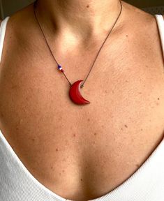 a woman wearing a necklace with a red crescent pendant