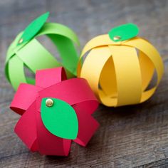 three colorful paper pumpkins sitting on top of a wooden table next to each other