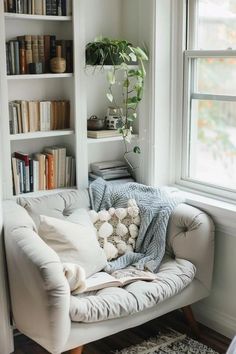 a white couch sitting in front of a window next to a book shelf filled with books