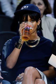 two women sitting next to each other at a basketball game drinking from glasses in front of them