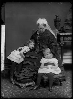 an old black and white photo of two women with three children sitting on a chair