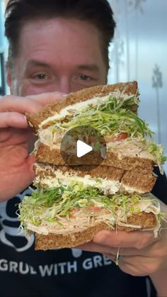 a man holding up a large sandwich with lettuce and tomato on it in front of his face