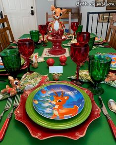 the table is set with green and red plates, silverware, and glassware