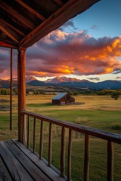 a wooden porch with a view of the mountains and sky at sunset or dawn,