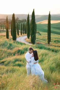 a man and woman standing in the middle of a lush green field with trees behind them