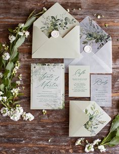 the wedding stationery is laid out with greenery