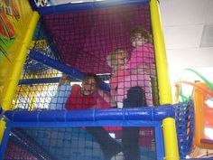 three children playing in a play area with blue and yellow mesh netting on the walls