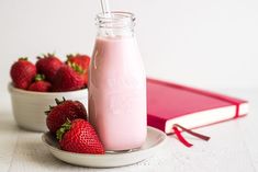 strawberries and milk are sitting on a plate next to a pink tray with a red book