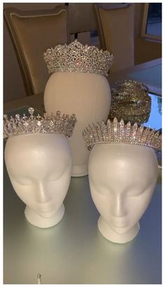 three white head vases sitting on top of a table with silver crowns in them