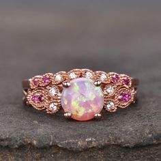 an opal and pink sapphire ring on top of a rock with white diamonds in the center