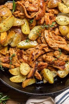 chicken and potatoes in a skillet on a wooden table with rosemary sprigs