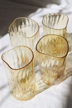 four yellow glass cups sitting on top of a white cloth covered tablecloth, with one empty cup in the middle