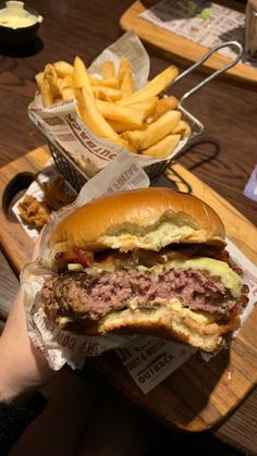 a person holding up a large sandwich and french fries in front of them on a table