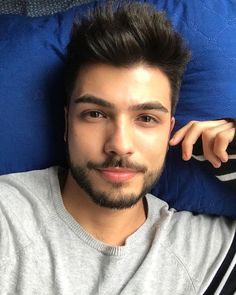 a man laying down with his hand on his head and looking at the camera while wearing a sweater