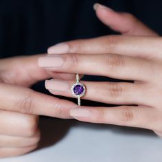 a woman's hand holding a ring with a purple stone