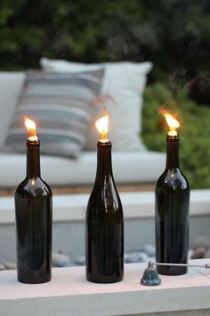 three wine bottles sitting on top of a table next to each other with candles in them