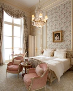 a bed room with a neatly made bed and two pink chairs next to a table