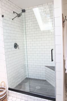 a walk in shower sitting next to a white tiled wall and floor with black accents