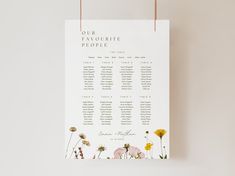 a wedding seating chart hanging from a string on a wall with dandelions and wildflowers