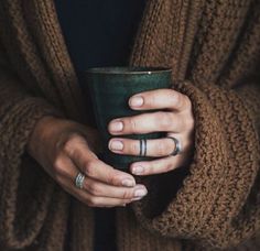 a woman holding a cup in her hands with two wedding rings on it's fingers