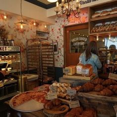 a woman standing in front of a bakery counter filled with breads and pastries