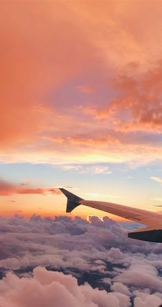 the wing of an airplane as it flies through the clouds at sunset or dawn with pink and blue hues