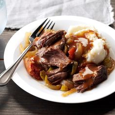 a white plate topped with meat and vegetables next to a glass of water on top of a wooden table