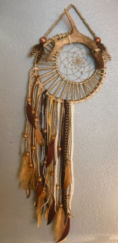 a wall hanging with feathers and beads on it's side in a room next to a white wall