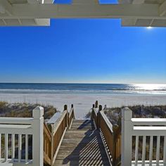 a wooden walkway leading to the beach with white railings and sand dunes in the background