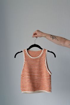 an orange and white striped shirt hanging on a hanger next to a person's arm