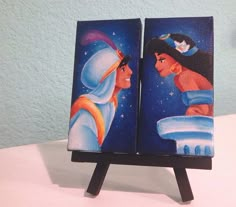 a couple of paintings sitting on top of a wooden stand