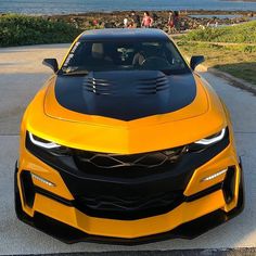 the front end of a yellow sports car parked on a road next to some water