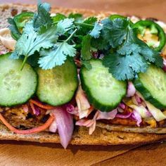 a sandwich with cucumbers, onions, and lettuce on it sitting on a wooden table