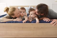 a man and woman kiss their two children on the bed while they lie next to each other